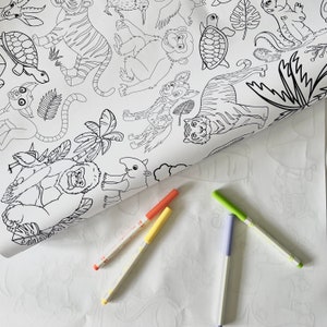 May include: A black and white colouring page featuring a variety of jungle animals, including tigers, monkeys, and birds. The page is rolled up and there are four coloured markers next to it.