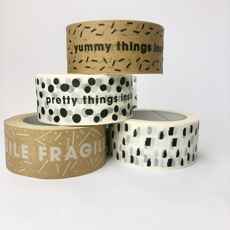 May include: Four rolls of brown and white patterned packing tape. The tape has different designs, including black dots, black lines, and black and white abstract shapes. The text on the tape reads "yummy things inside", "pretty things inside", and "fragile".