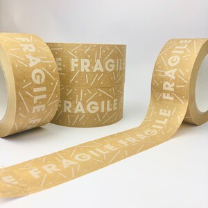 May include: Three rolls of brown packing tape with the word "FRAGILE" printed in white on the tape. The tape has a pattern of white lines and dots on a brown background.