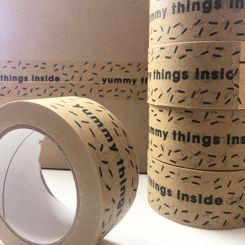 May include: Close-up of a roll of brown packing tape with the text "yummy things inside" printed on it. The tape has a black and white confetti pattern.