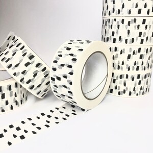 May include: Rolls of white washi tape with a black and gray abstract pattern. The tape is unrolled and shows the pattern.