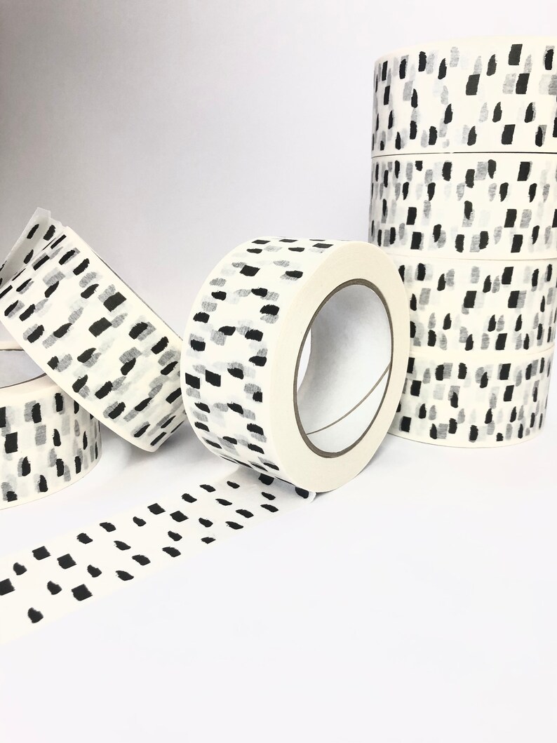 May include: Rolls of white washi tape with a black and gray abstract pattern. The tape is unrolled and shows the pattern.