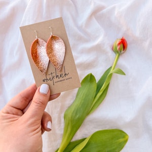 May include: A pair of rose gold and silver leaf-shaped earrings on a brown card with the text "white birch handmade goods".