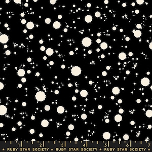 May include: Black fabric with a pattern of off-white paint splatters. The splatters vary in size and density, creating a speckled effect. The fabric has a ruler along the bottom with the text "RUBY STAR SOCIETY".