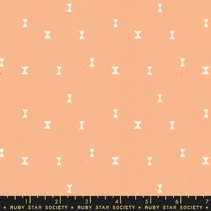 May include: Peach-colored fabric with a repeating pattern of small, off-white bow tie shapes. The fabric has a slightly textured appearance. A ruler is at the bottom of the image, with the text "RUBY STAR SOCIETY".