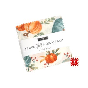 May include: A bundle of fabric squares with a fall-themed print featuring orange pumpkins, teal leaves, and red berries on a cream background. The fabric is wrapped with a white band that reads "I LOVE Fall MOST OF ALL!" by Deb Strain.