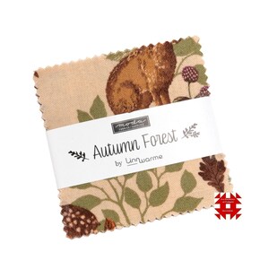 Op de afbeelding: Een stapel stoffen vierkanten met een beige achtergrond en een herfstbosontwerp. De stof heeft een bruin hert, groene bladeren en bessen. Het witte label luidt "Autumn Forest by Linnwarme."
