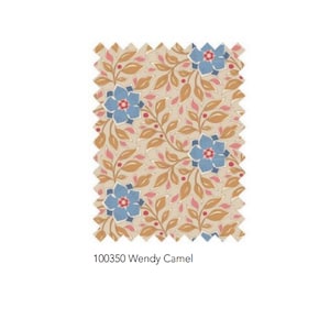 May include: A fabric swatch featuring a floral pattern with blue flowers, brown leaves, and pink accents on a beige background. The text "100350 Wendy Camel" is printed at the bottom. The edges of the swatch are zig-zagged.