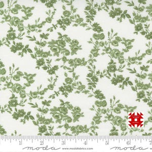 May include: White fabric with a repeating pattern of green roses and leaves. The floral design is detailed and covers the entire surface. A ruler is at the bottom, with the word "moda" printed on it.