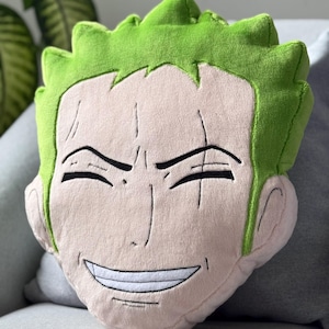 Könnte beinhalten: Ein Plüschkissen in Form einer Comicfigur mit grünen Haaren und einem lächelnden Gesicht.