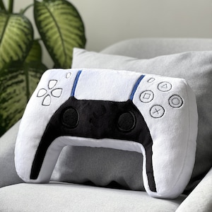 May include: White plush pillow shaped like a Playstation 5 controller. The pillow has black buttons and a blue accent.