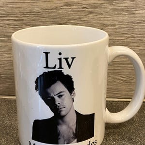 May include: White ceramic mug with a black and white photo of a person with the text "Liv Mrs Harry Styles" printed on it.