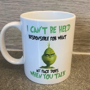 May include: White ceramic mug featuring a green Grinch illustration and the text "I CAN'T BE HELD RESPONSIBLE FOR WHAT MY FACE DOES WHEN YOU TALK". The mug has a curved handle.