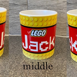 May include: A white ceramic mug with a yellow and red LEGO design. The mug features a LEGO minifigure wearing a red hard hat and a yellow construction vest. The text "LEGO" and "Jack" are printed in black on the mug.