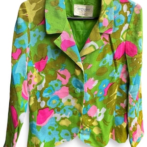 May include: A vintage blazer with a vibrant floral pattern in shades of green, pink, blue, and yellow. The jacket features a classic collar, two buttons, and long sleeves. The label reads "sportempos".