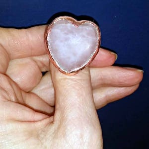 Pode incluir: Um anel em forma de cora&ccedil;&atilde;o com uma pedra de quartzo rosa engastada em uma moldura de metal de cor cobre.