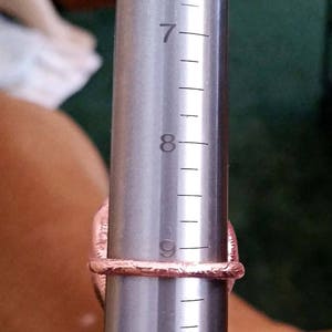Pode incluir: Um close-up de um calibrador de an&eacute;is com um anel rosa nele. O calibrador de an&eacute;is &eacute; marcado com os n&uacute;meros 7, 8 e 9.