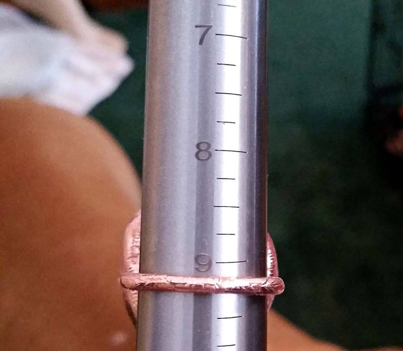 Pode incluir: Um close-up de um calibrador de an&eacute;is com um anel rosa nele. O calibrador de an&eacute;is &eacute; marcado com os n&uacute;meros 7, 8 e 9.