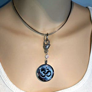 May include: A silver chain necklace with a silver Om symbol pendant and a heart-shaped clasp. The pendant has a small opening for essential oils.