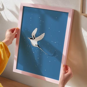 Peut inclure: Une impression d'art encadrée représentant un oiseau stylisé en vol sur un fond bleu parsemé de points blancs. L'oiseau est principalement blanc avec des détails noirs et une longue queue. Le cadre est rose clair.