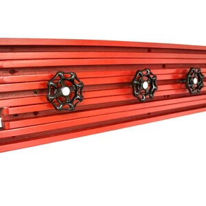 May include: Red wooden wall mounted coat rack with four black metal hooks shaped like industrial valve wheels.