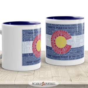May include: Two white ceramic coffee mugs with blue rims. The mugs feature a design of the Colorado state flag with the names of mountains in the state printed around the flag. The text on the mugs reads "Missouri Mountain, Conundrum Peak, Mount Torreys Peak, Wilson Peak,  Peakshava, Capitol Peak, San Luis Peak, Humboldt Peak, Democrat Mountain, Mount Harvard, Blanca Peak, Wetterhorn, Mount Bierstadt, Mount Sherman, Sunshine Peak, Mount Evans,  Mount Lincoln, Mt. Yale,  Mount Cameron, Maroon Peaks, Mount Handies Peak, Princeton, Challenger Point, Mount Massive, Mount of the Holy Cross, El Diente Peak, Culebra Peak, Kit Carson Peak."