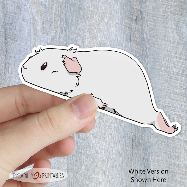 May include: White sticker of a cartoon guinea pig with pink ears and a white body. The sticker is being held by a hand.