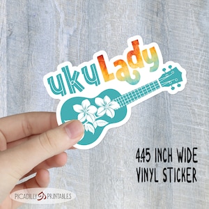May include: A vinyl sticker featuring a teal ukulele shape with white flowers and the words "uku Lady" in colorful lettering. The sticker is 4.45 inches wide.