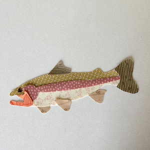 May include: A colorful fish applique made from patterned fabric. The fish features a green polka dot top, a pink floral middle, and a cream floral bottom. The fins and tail are brown with vertical stripes.
