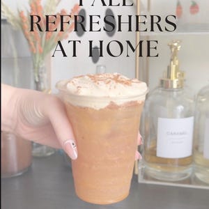 May include: A clear plastic cup filled with an amber-colored iced beverage topped with a thick layer of white foam and a dusting of brown spice. The text E-BOOK FALL REFRESHERS AT HOME and BECCA BREWS is visible on the digital overlay of the image.