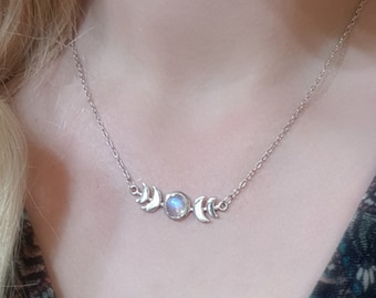 May include: Silver-toned necklace featuring a crescent moon and a central moonstone pendant. The necklace is worn around the neck and is displayed against a patterned top. The design is delicate and celestial, suitable for everyday wear.