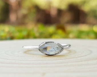 May include: A silver ring featuring a clear marquise-shaped gemstone. The ring is resting on a wooden surface.
