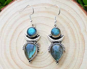 May include: A pair of silver dangle earrings with iridescent blue and green labradorite stones. The stones are set in a crescent moon design.