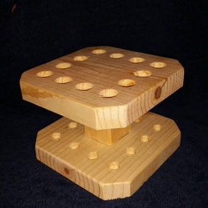 May include: A wooden tool holder with multiple holes for storing tools. The holder is made of light brown wood and has a two-tiered design.