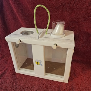 May include: White wooden bee observation box with three compartments, a clear plastic lid, and a green rope handle. The box has a bee illustration on the front.