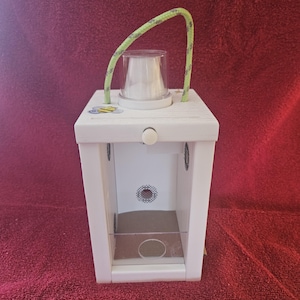 May include: White wooden bee house with a clear plastic window and a green rope handle. The house has a small bee sticker on the front.