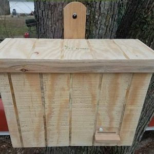 May include: A wooden birdhouse with a hinged lid and a small opening for birds to enter. The birdhouse is mounted on a tree trunk and has a small wooden sign on the front that says "Tree Hugger" with a tree branch design.