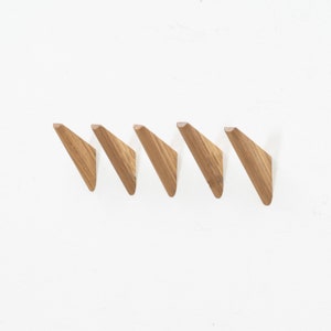 May include: Five wooden wall hooks in a row, each shaped like a triangle with a pointed tip. The hooks are a light brown color and are mounted on a white wall.