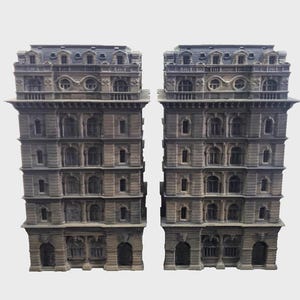 May include: Two miniature, detailed building models. Each model is a multi-story structure with a gray facade, arched windows, and a dark gray roof. The buildings have ornate architectural details, suggesting a classical or European style.