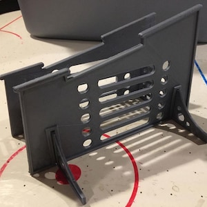 Può includere: Un supporto in plastica grigia con un motivo a griglia e quattro gambe. Il supporto è progettato per tenere gli oggetti in posizione verticale.