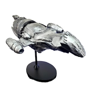 May include: A detailed silver-colored model spaceship, mounted on a black stand. The spaceship features intricate designs, including multiple engines and a detailed cockpit area. The model is a collectible item, perfect for sci-fi enthusiasts.