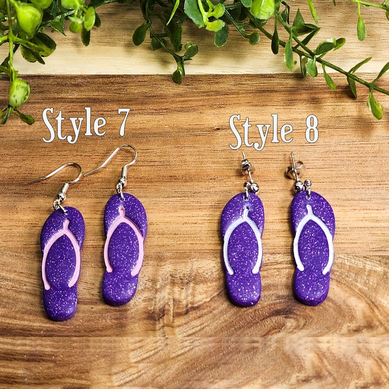May include: Two pairs of purple glitter flip flop earrings with white or pink wishbone designs. The earrings are labeled "Style 7" and "Style 8".