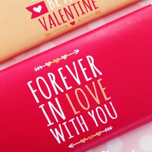Op de afbeelding: Rode en gouden Valentijnsdag-chocoladeverpakking met de tekst "FOREVER IN LOVE WITH YOU" en gouden hartjes en pijlen.