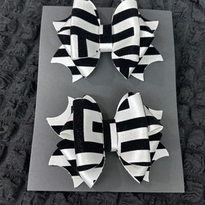 May include: Two black and white patterned hair bows with a geometric design. The bows are made of satin and velvet.