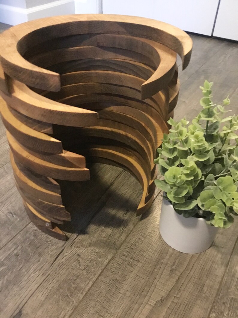 May include: A unique wooden side table with a spiral design. The table is constructed from curved, light brown wooden pieces stacked to create a cylindrical shape. A small potted plant with green leaves sits beside the table.