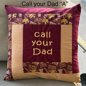 May include: A maroon and tan pillow with the words "Call your Dad" embroidered in gold thread. The pillow is decorated with a repeating pattern of Texas State Bobcats logos.