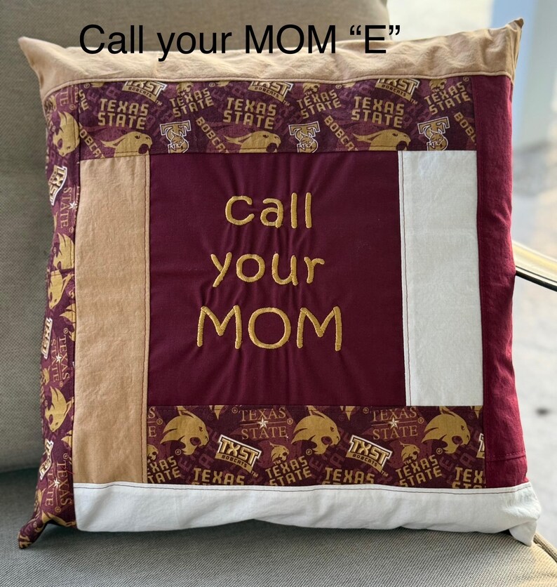 May include: A maroon and tan pillow with a white panel in the center. The pillow has a gold embroidered message that says "Call your MOM" on the maroon panel. The tan panels have a repeated pattern of a maroon and gold Texas State Bobcat mascot.