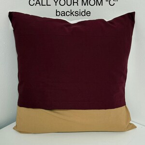 May include: A burgundy and tan pillow with the text "CALL YOUR MOM "C"" printed on the front. The back of the pillow is shown in the image.