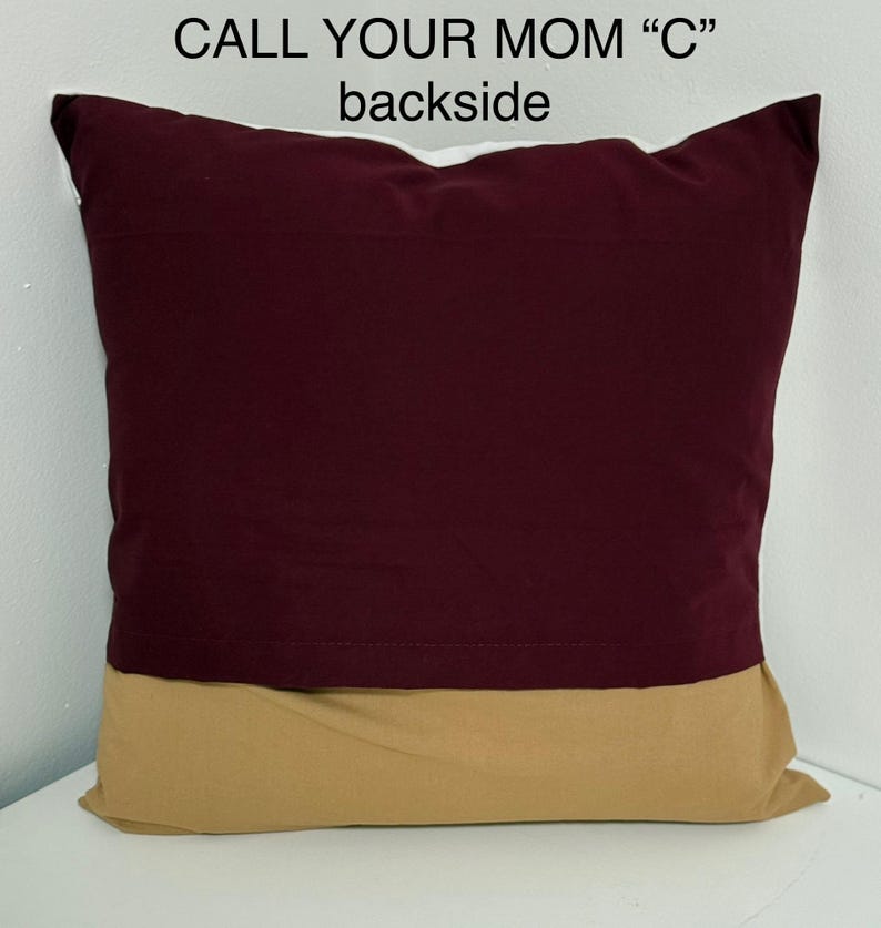 May include: A burgundy and tan pillow with the text "CALL YOUR MOM "C"" printed on the front. The back of the pillow is shown in the image.