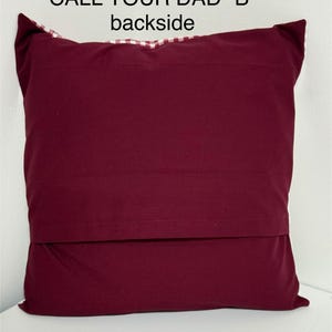 May include: Burgundy red pillow with a white and red checkered fabric on the back. The pillow has the text "CALL YOUR DAD "B"" printed on the front.